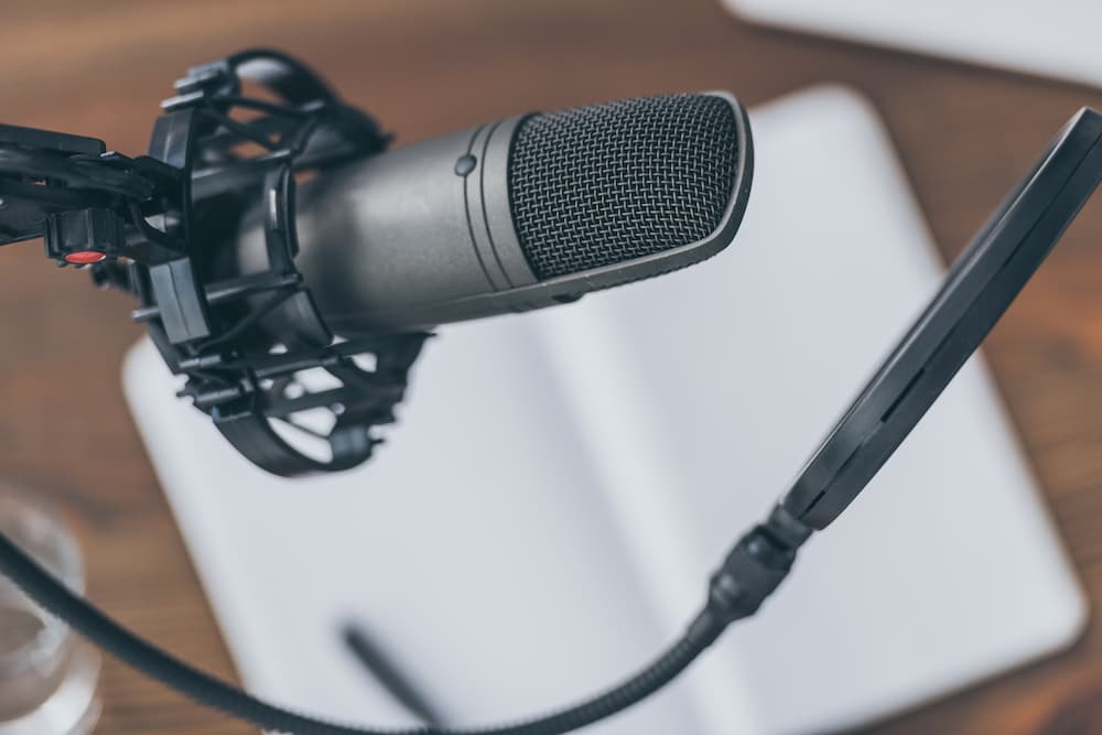 A microphone on a boom arm hovering over a blurred focused notebook sitting on a desk